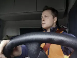 Truck Driver Wearing a High Visibility Vest and Red Seat Belt view from the front with the Driver looking Right with the interior of the Semi Truck Lockers behind.