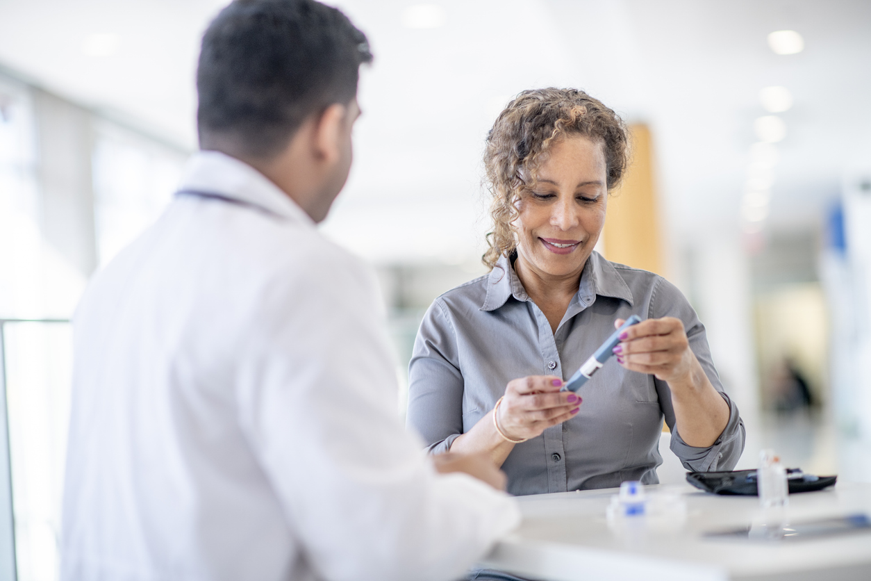 A female adult is at a medical check up appointment for a diabetic medical condition. She is holding a insulin pen that is used to do a medical injection. She is smiling.