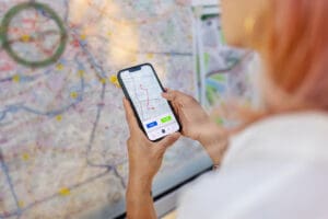 Over the shoulder view of female commuter holding a phone with route map and looking at the train network map on train station. Woman standing by city map on station and using smart phone to plan route.